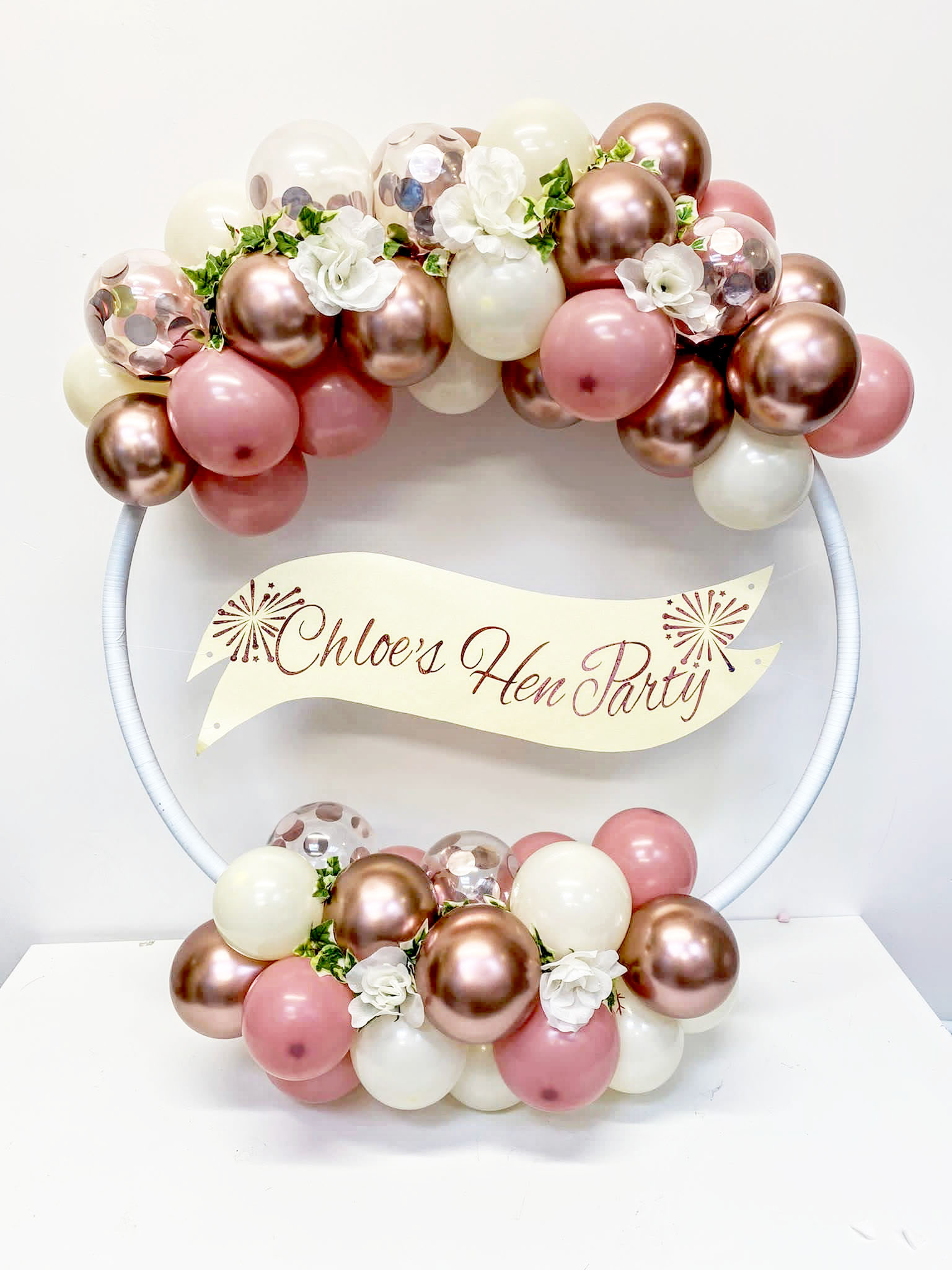 A balloon hoop with personalised banner for Chloes Hen Party in Rose Gold, Cream mini balloons and floral accesories all elegantly styled on a hoop shape