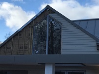 Shaped fixed window with mullion in centre, cladding fitted around window in gable end