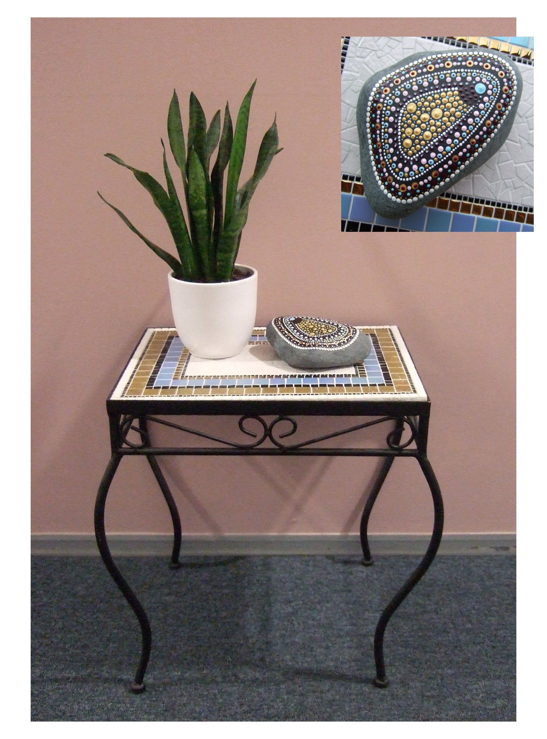 Een klein mozaiektafeltje met wit, lichtblauw en goud glasmozaiek. Op de tafel ligt een kei die is gedecoreerd met stippen in dezelfde kleuren als het tafeltje. Daarnaast staat een klein plantje in een wit potje.