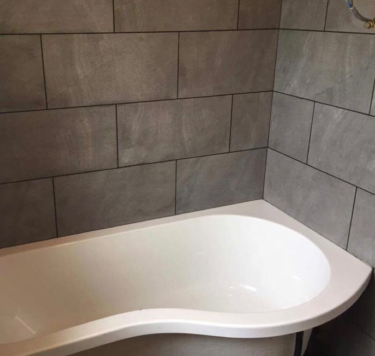 Large rectangular tiles fitted around a modern curved bath