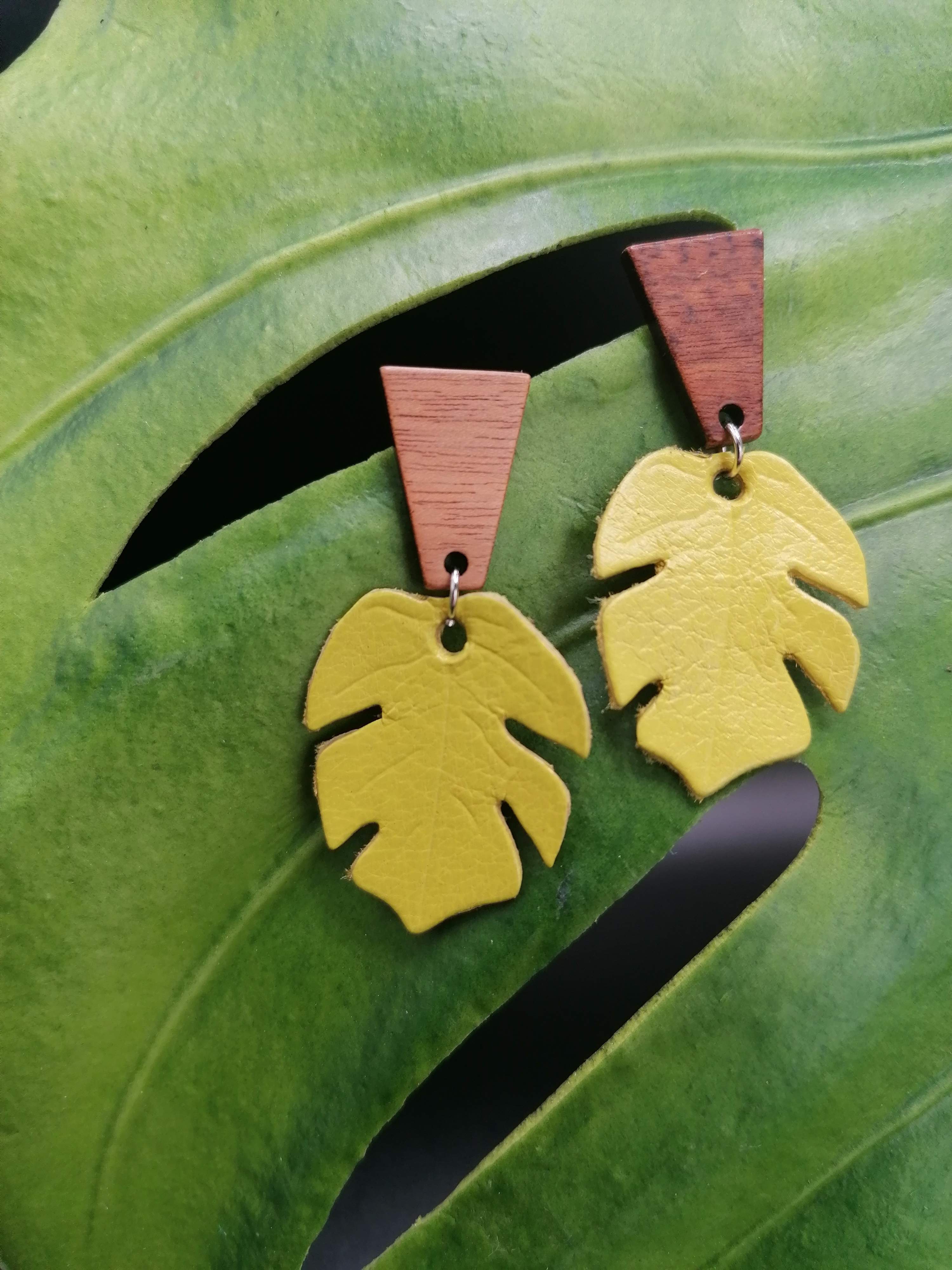 Small leather monstera leaves on geometric wooden studs hanging from a leaf