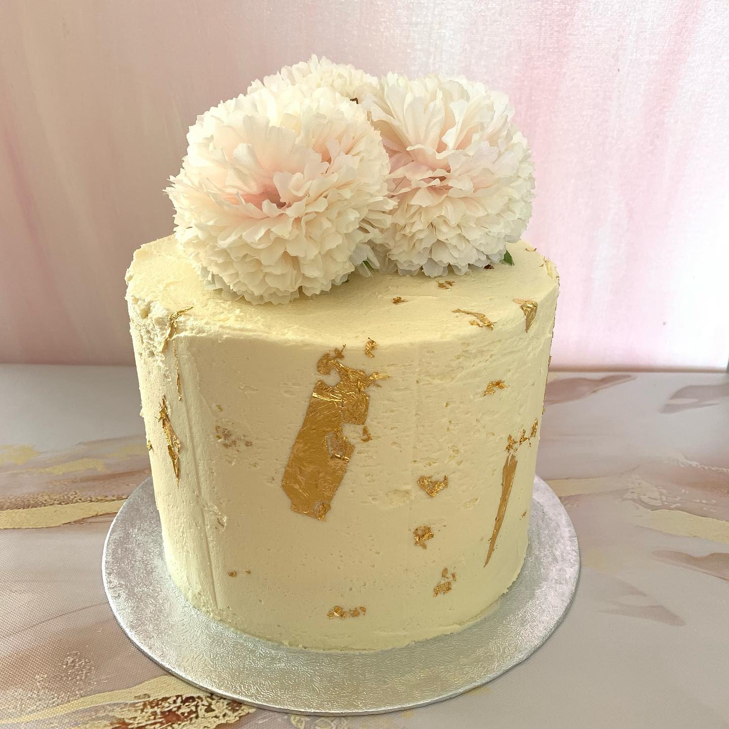 Cake with cream coloured frosting, splashes of gold leaf and faux flowers on top