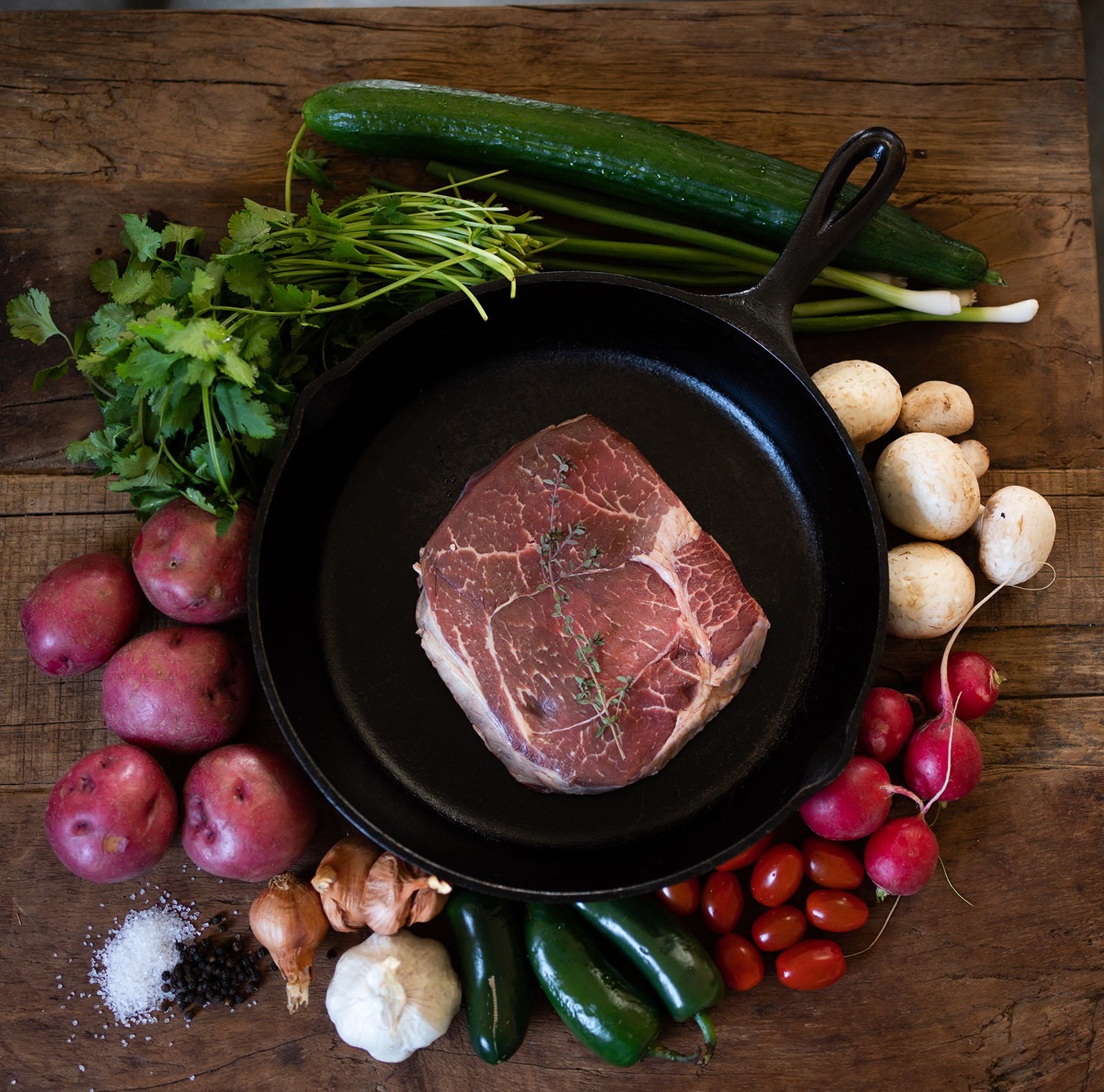 boneless chuck roast in a cast iron skillet and surrounded by garden vegetables.