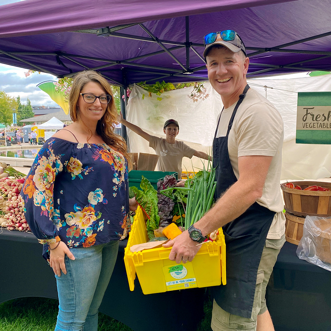 A happy customer at the Cobourg Farmer's Market receiving their weekly CSA Farm box of vegetables