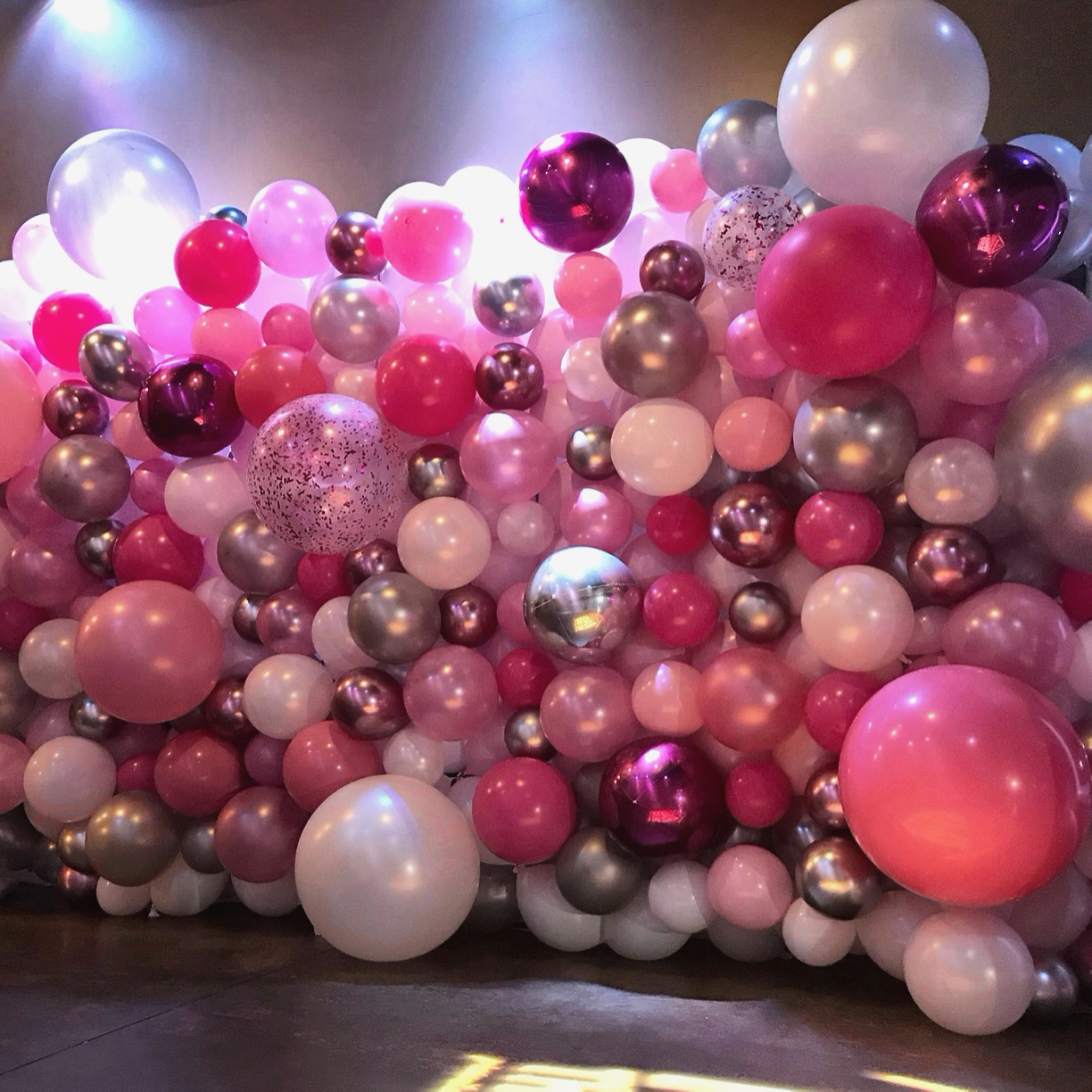 Balloons in multiple shades of pink with white and chrome silver organic balloon wall.