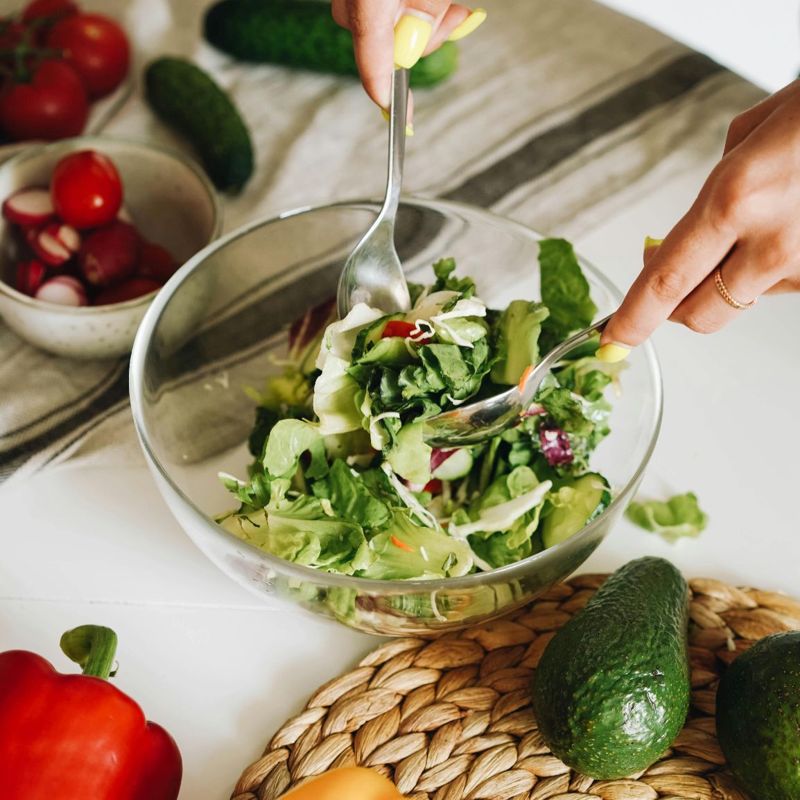 Someone preparing a salad in a bowl using fresh organic salad greens, cucumbers, and radishes.