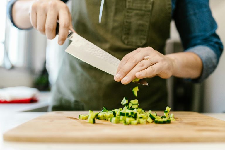 A person chopping vegetables in on a kitchen counter to prepare a meal