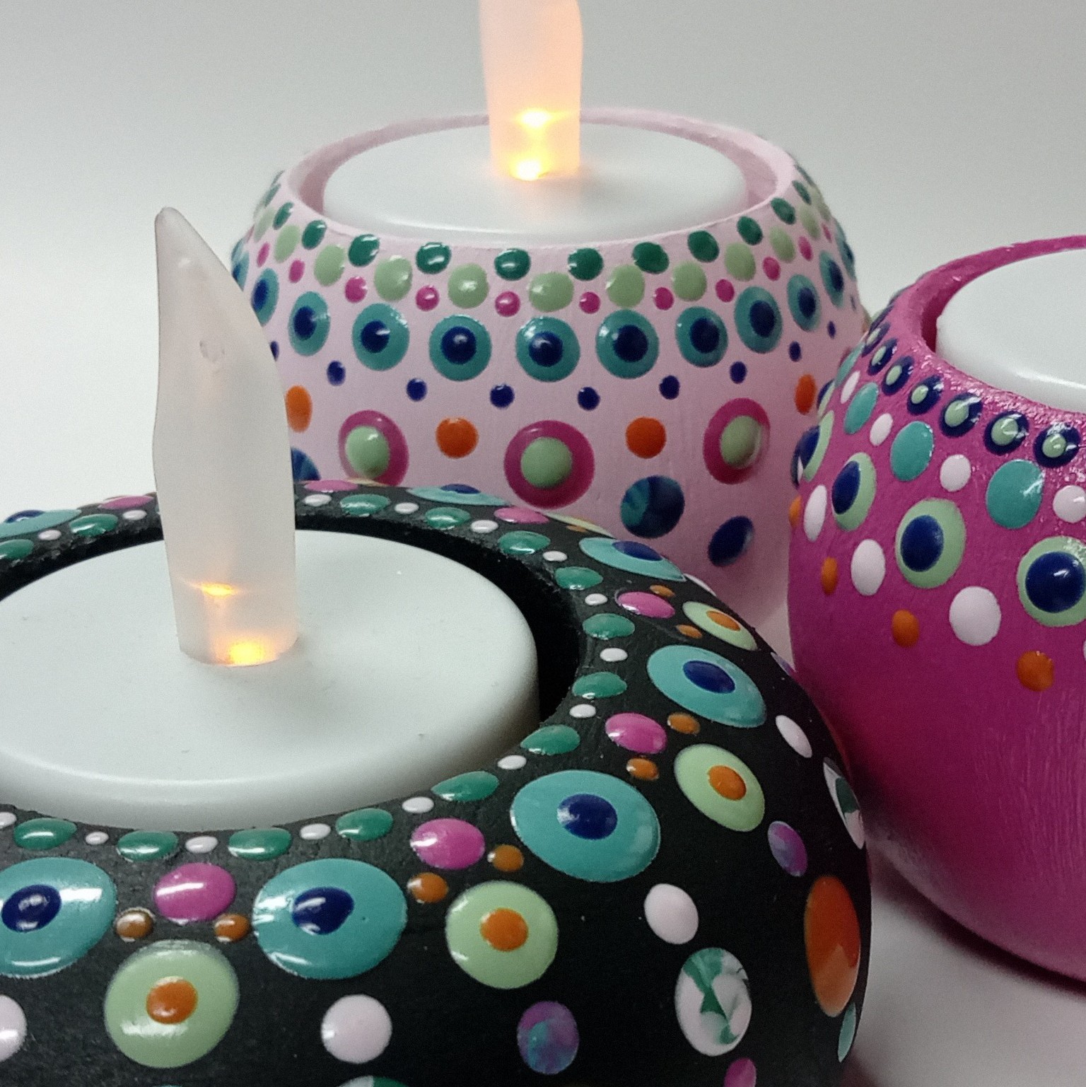 Drie waxinelichthouders met meerkleurige dots, iriserende dots en diverse kleuren als ondergrond.