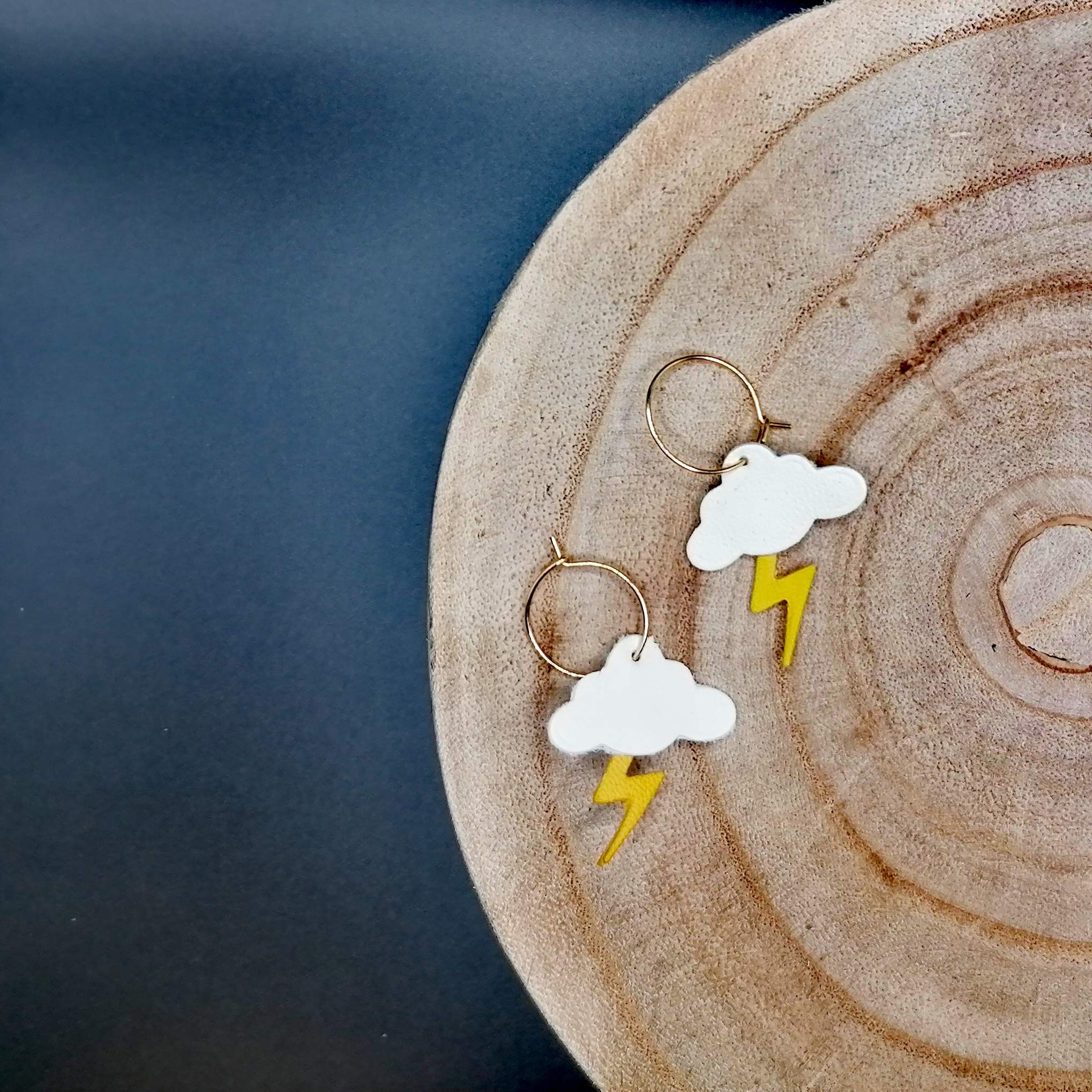 Small white leather clouds with yellow leather lightning bolt, on gold hoops. Sitting on wood slice