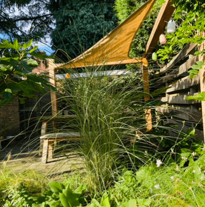 De eethoek is afgeschermd door een vaste plantenborder en een hoek pergola