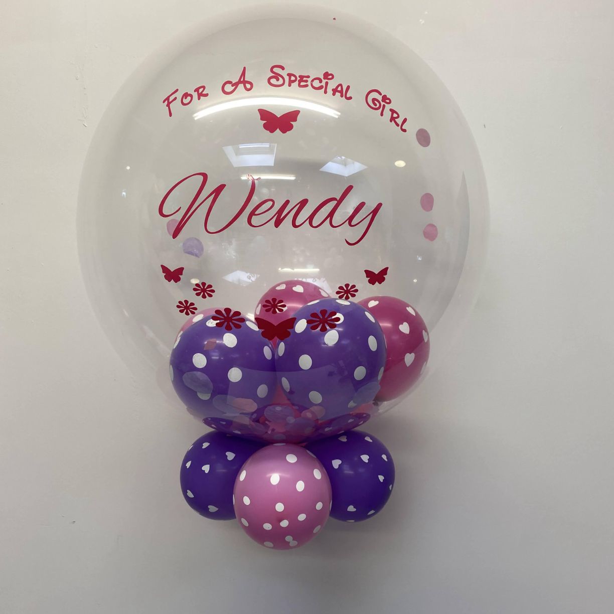 A personalised clear Bubble balloon with mini polka dot balloons inside the balloon and a pink For a Special Girl Wendy printed on the clear bubble balloon