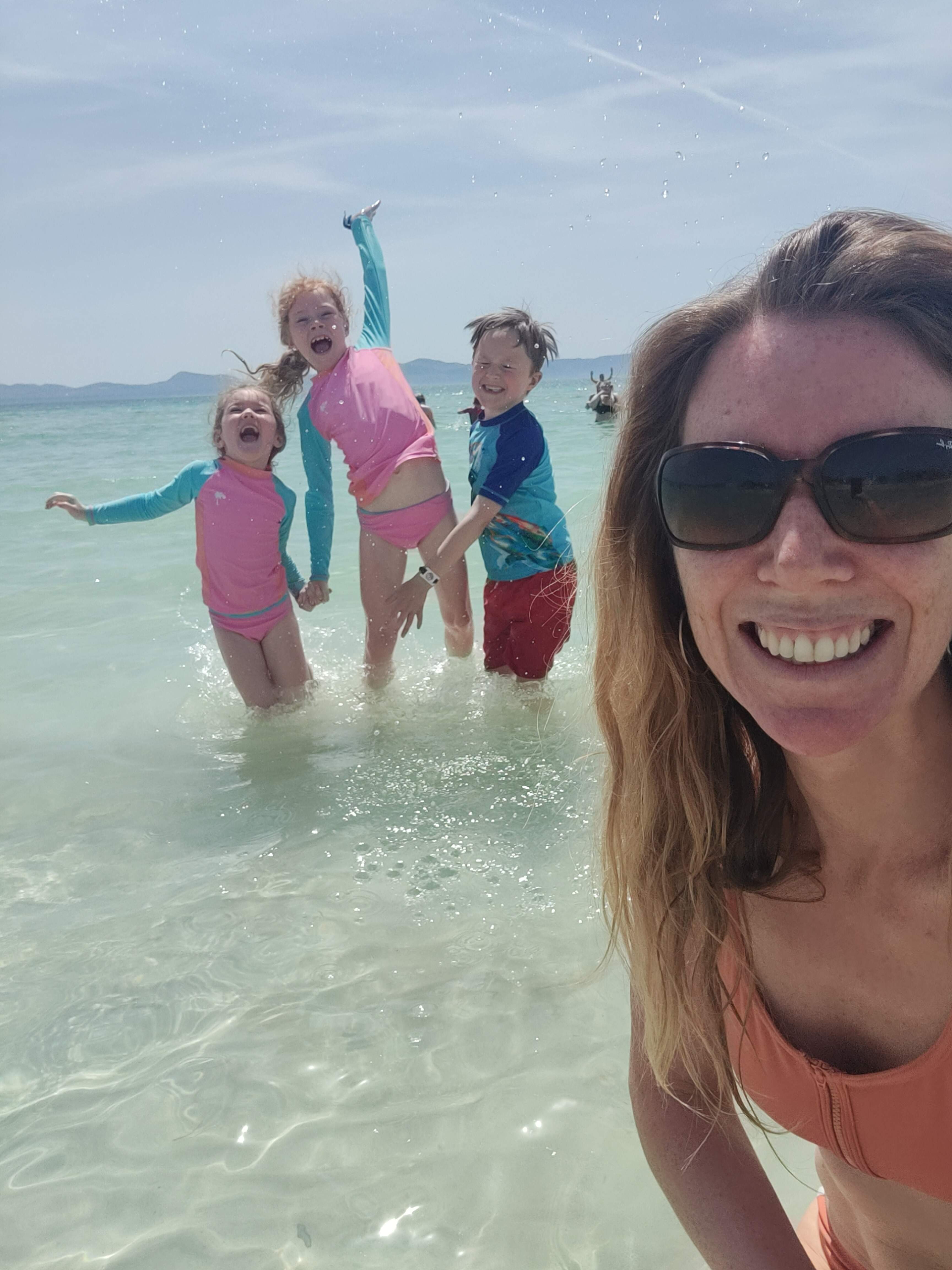 A mum smiling and happy with her children in the sea. Work with Bump and Beyond Wellness. Private coaching and 8 week programme for new mothers.