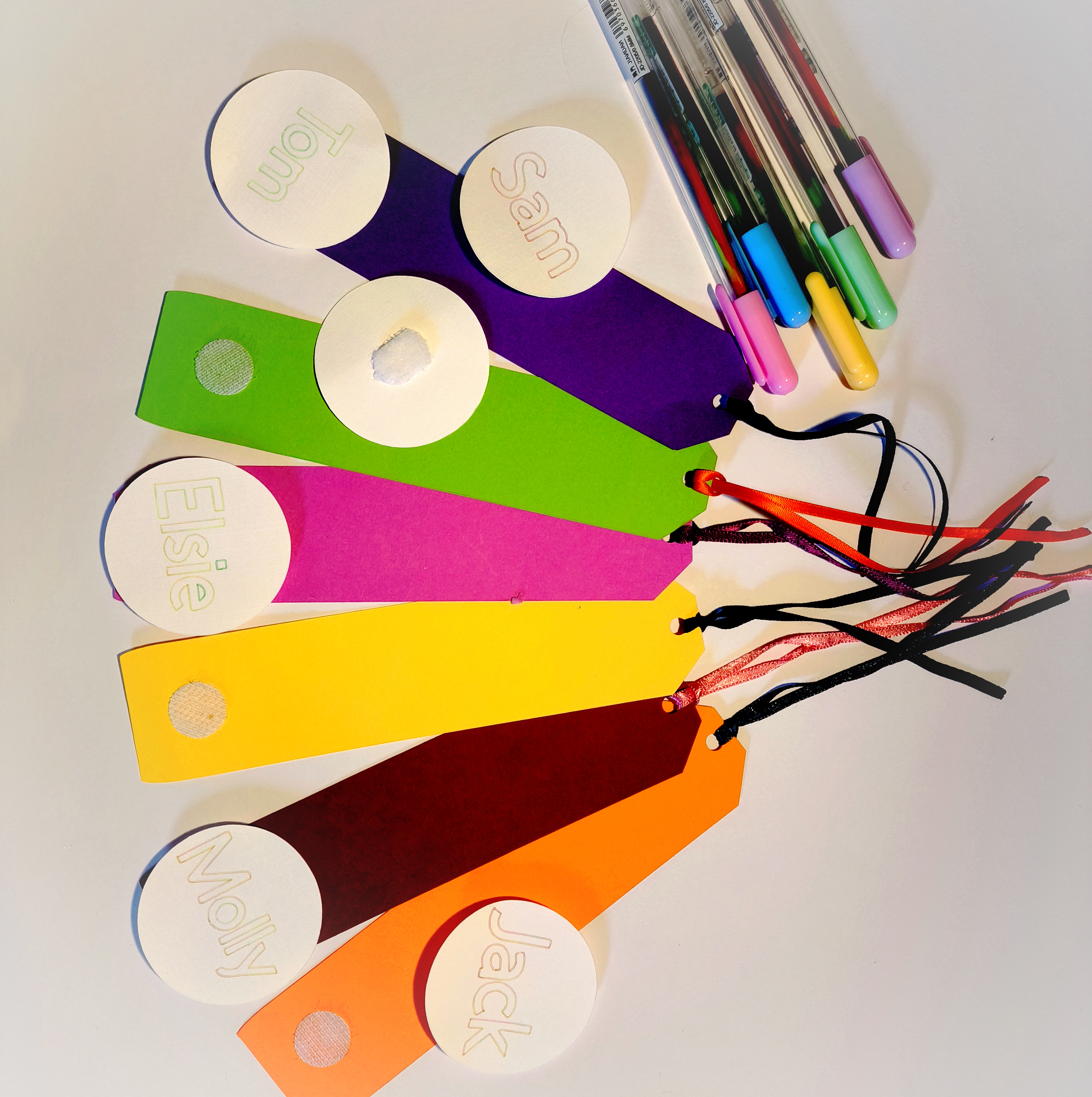 Brightly coloured bookmarks with ribbons attached and removable, circular, name tags attached with velcro