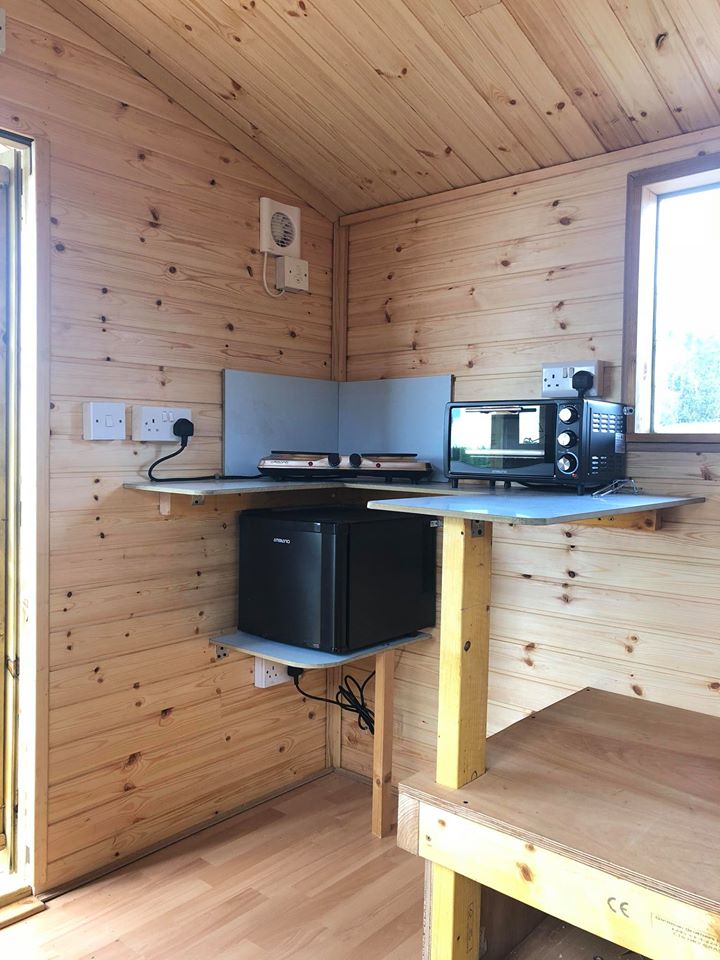 The kitchen corner of a glamping shed with fridge, microwave and cooking plates