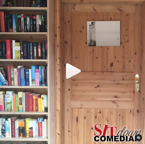 Video vom Sit down Comedian, zu sehen eine geschlossene Holztür, daneben ein Büchergestell.