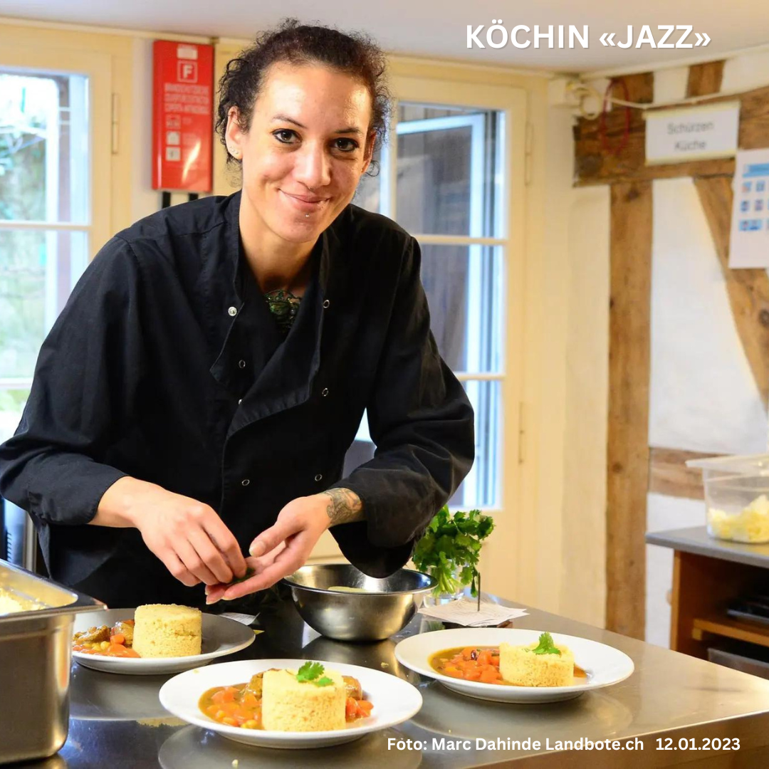 Ein Koch in schwarzer Uniform garniert Teller mit Couscous und Eintopf in einer gut beleuchteten Küche. In der Nähe stehen verschiedene Küchenutensilien. Der Text auf dem Bild lautet 'KÖCHIN «JAZZ»' und das Aufnahmedatum ist der 12.01.2023.