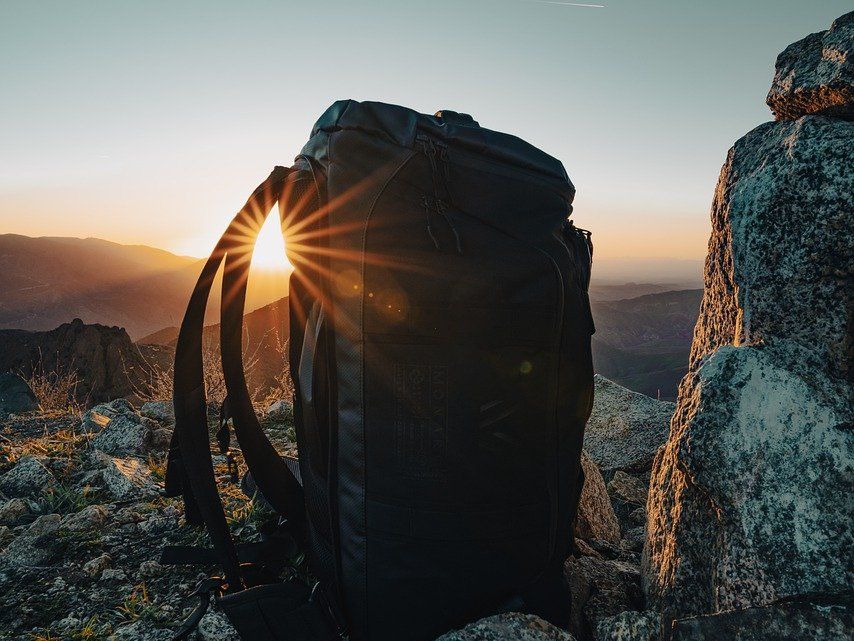 Rucksack steht auf Steinen und die die Sonne scheint und der Himmel ist blau.