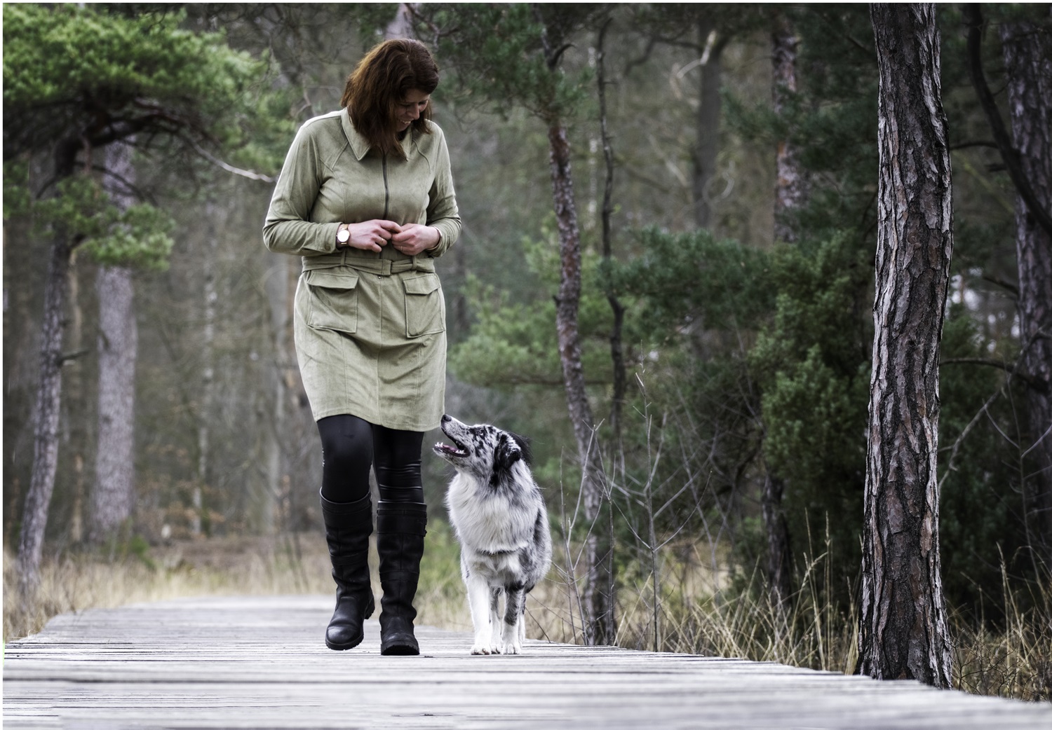 Een Gedragstherapeut voor honden die samen met haar Australian Shepherd loopt in een natuurgebied.