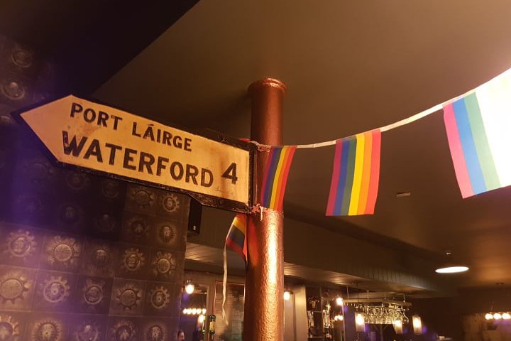 Rainbow Bunting draped over a black and white waterford road sign in Downes bar, Thomas Street