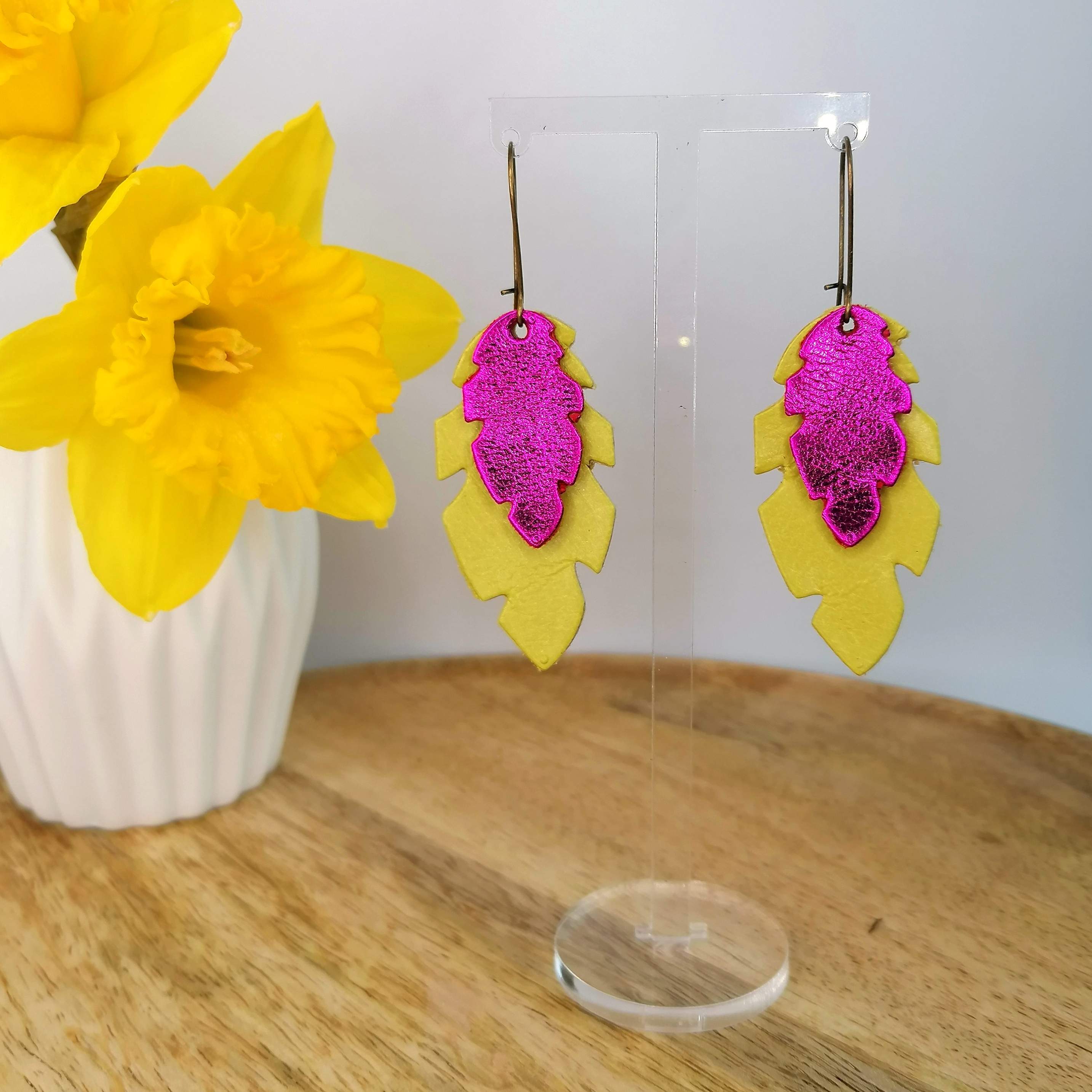 Yellow and pink double leather feathers, hanging from a stand on a wooden tray beside a daffodil